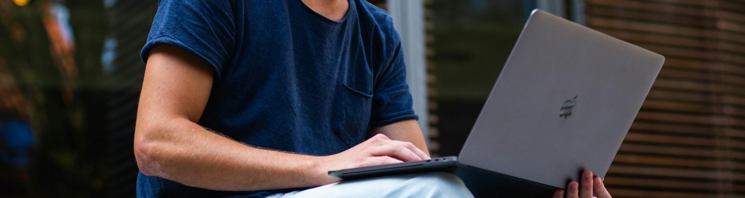 a man holding his laptop and typing on the keyboard 